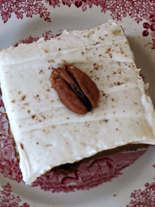 A bar cake with cream cheese frosting and a pecan on top sitting on a red and white plate. 