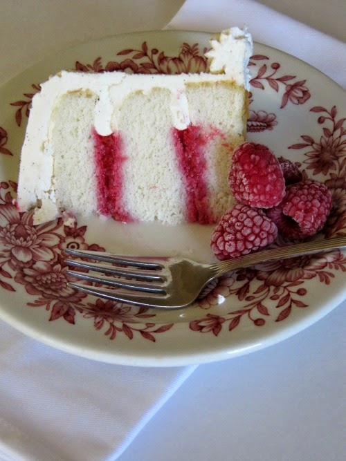 A slice of white cake with raspberry filling on a red and white flower cake. 