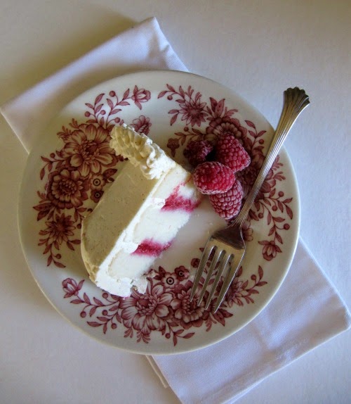 A slice of white cake filled with raspberries on a red and white transfer ware plate. 
