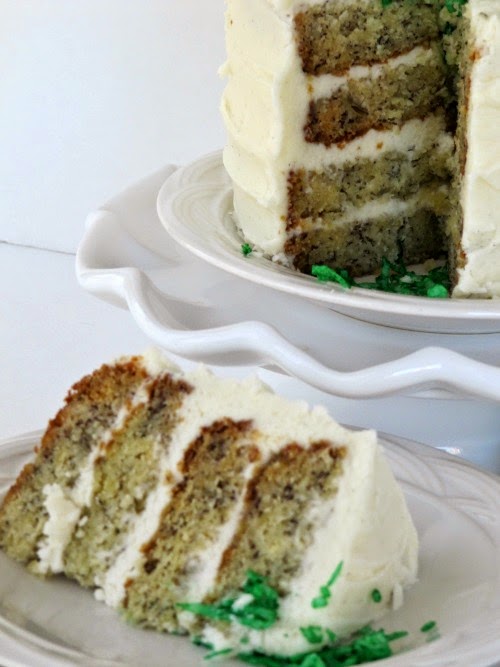 Cake frosted with green coconut nut nest and 3 egg candies on a white cake plate with ruffles.