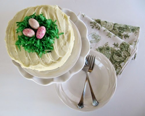 White frosted cake decorated with green coconut to make a nest and 3 pink eggs.