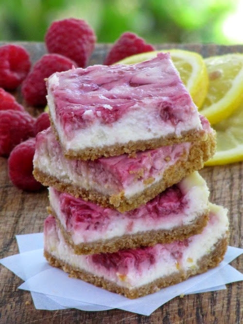 Raspberry swirled lemon cheesecake bars on a stack surrounded by lemon slices and fresh raspberries.