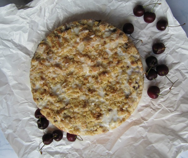 Cherry coffeecake with cherries on a white piece of parchment paper.