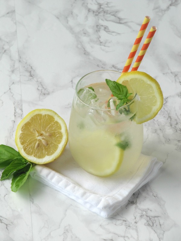 Basil lemonade in a glass with an orange and yellow stray.