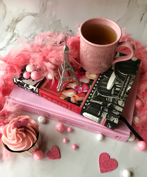 Two pink books with a pink mug of tea, a fronted pink cupcake and a small Eiffel Tower. 
