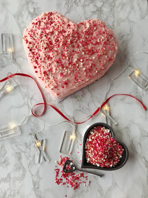 A pink heart shaped cake with sprinkles.