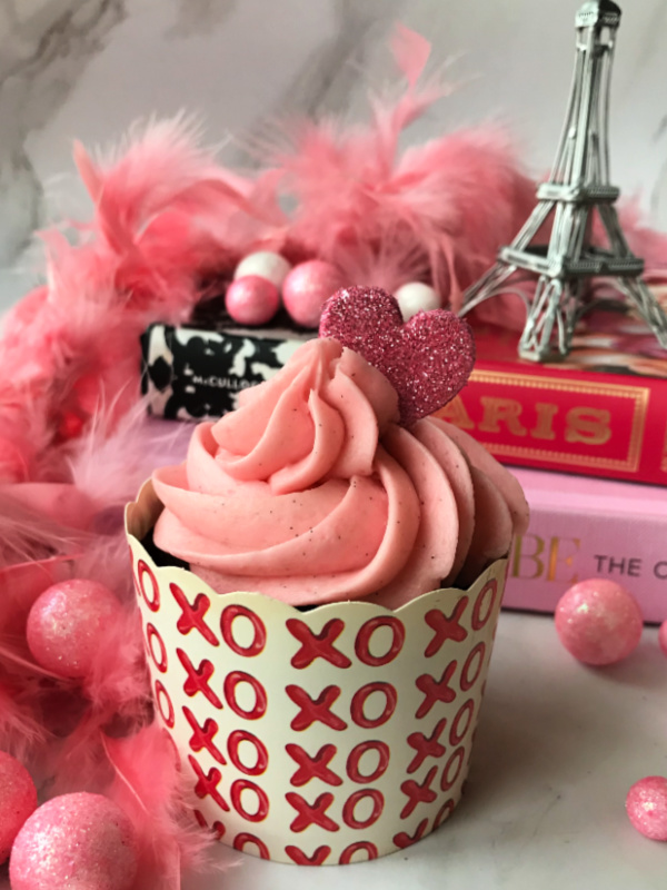 Valentines cupcake with pink frosting in front of pink books with an Eiffel Tower on top