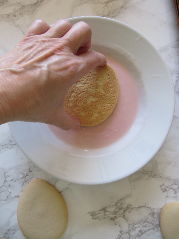 Hand dipping cookie into frosting