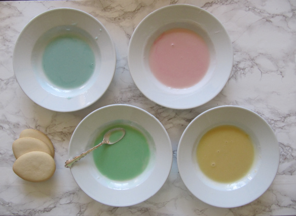 pastel pink green blue and yellow bowls of frosting with egg cookies