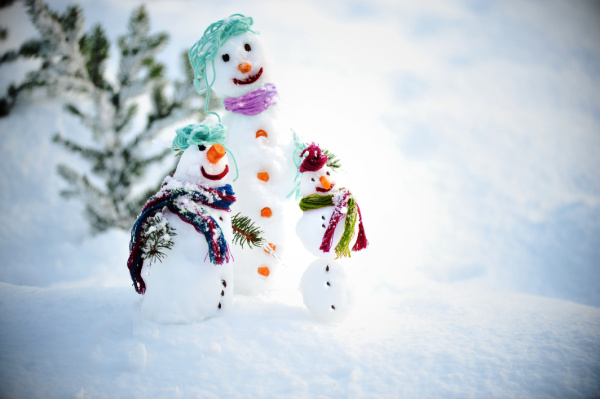 threes miniature snowmen in the snow with a tree in the background, 