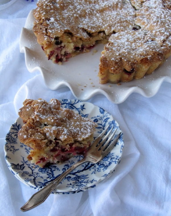 cranberry breakfast cake on blue and white plate with the rest of the cake on a white cake plate