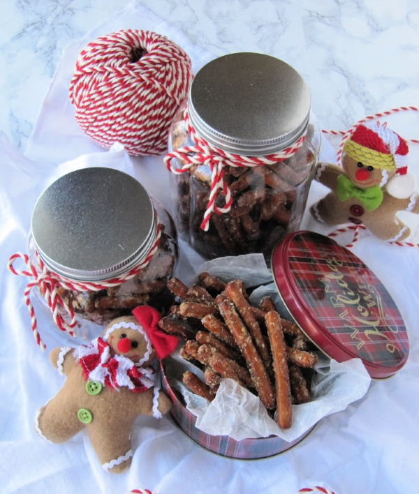 Two glass jars filled with pretzels and red twine wrapped around them with a christmas canister filled with pretzels and two lies stuffed gingerbread men sitting next to it