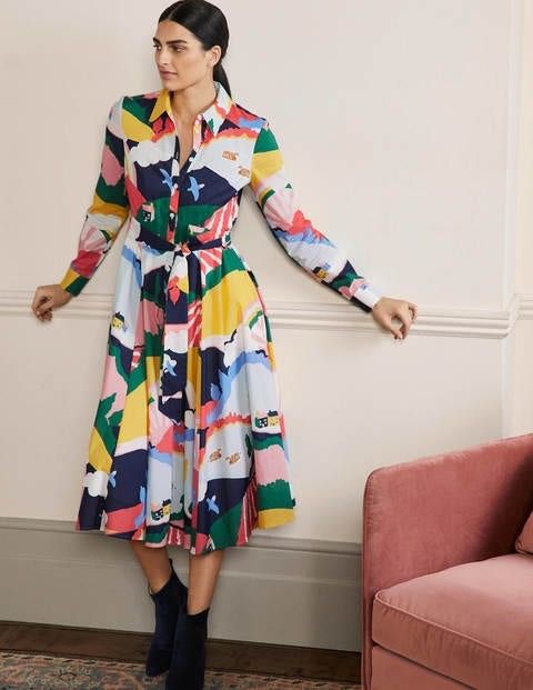 Woman standing with arms outstretched leaning against a wall in a colorful shirtdress