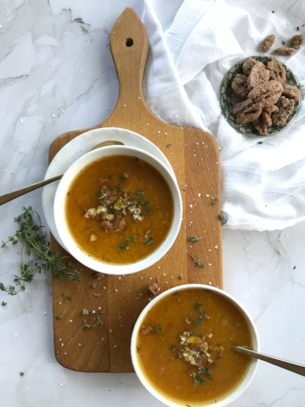easy-roasted-butternut-squash-pumpkin-soup-in-white-bowls-sitting-on-a-brown-cutting-board-with-a-white-cloth-in-the-right-hand-corner-and-a-small-bowl-of-pecans