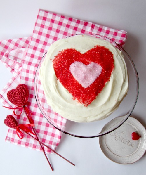 February is the month of love. chocolate-cake-buttercream-frosting with a Fred and pick sprinkle heart on a pink gingham napkin with two read hearts on sticks next to it