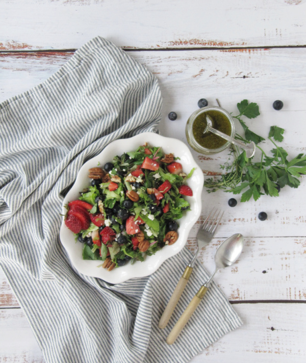 Strawberry and Fresh Herb Salad with Blueberries and Feta on a white plate sitting on a blue and white stripped towel