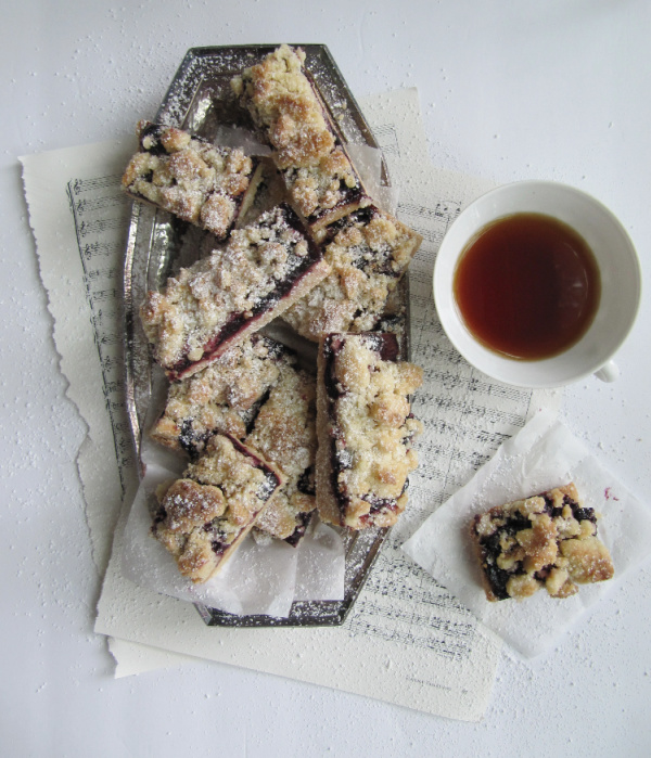  roasted cherry streusel bars in a silver tray sitting on sheet music with a cup of tea in a white cup