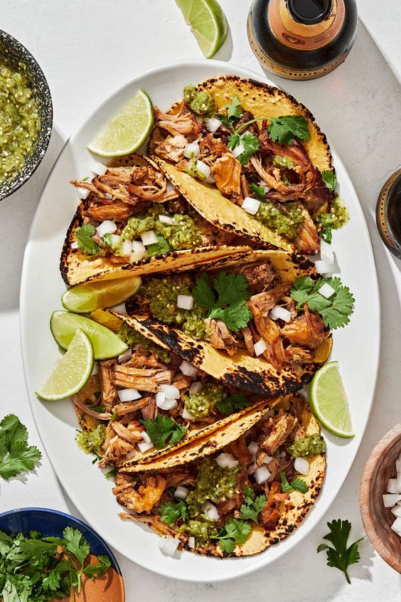 a white platter of crispy carnitas tacos with lime garnish