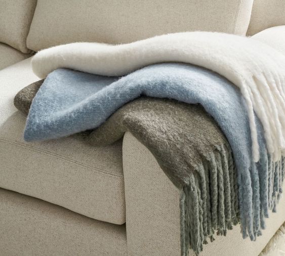 ivory, light blue and gray throw blankets on a ivory sofa.