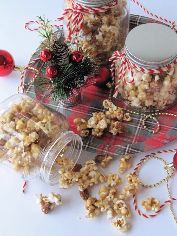 caramel-corn in three glass jars on a plaid tin tray. 