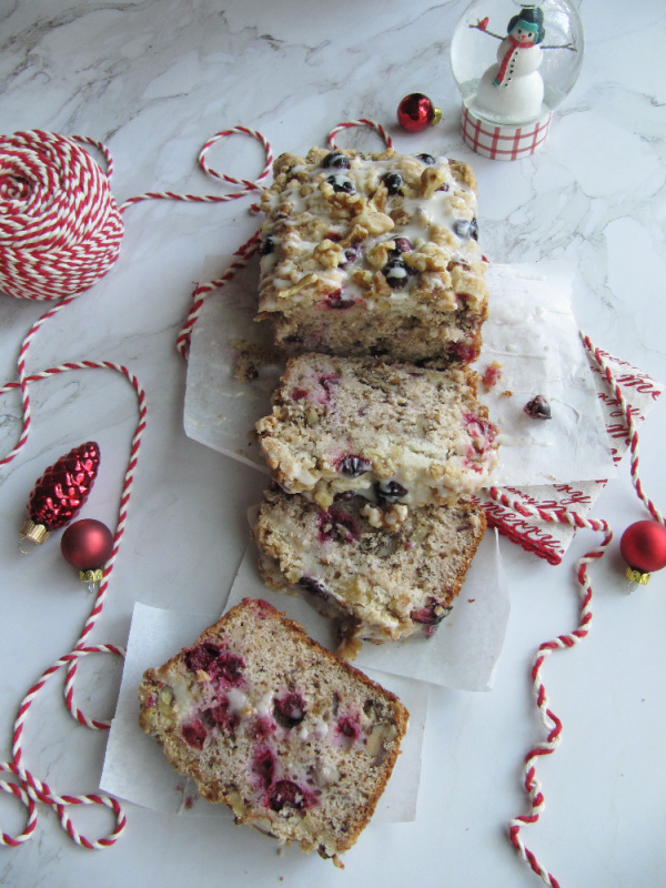cranberry-walnut-loaf-wrapped-in-white-paper-and-tied-with-red-and-white-string-on-a-white-piece-of-marble-with-scattered-christmas-bulbs-a-snow-globe-and-string-b