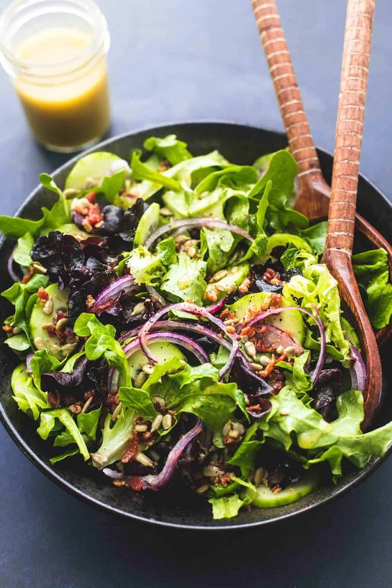 Tossed green salad with red onions in a brown bowl and salad utensils on the right side.