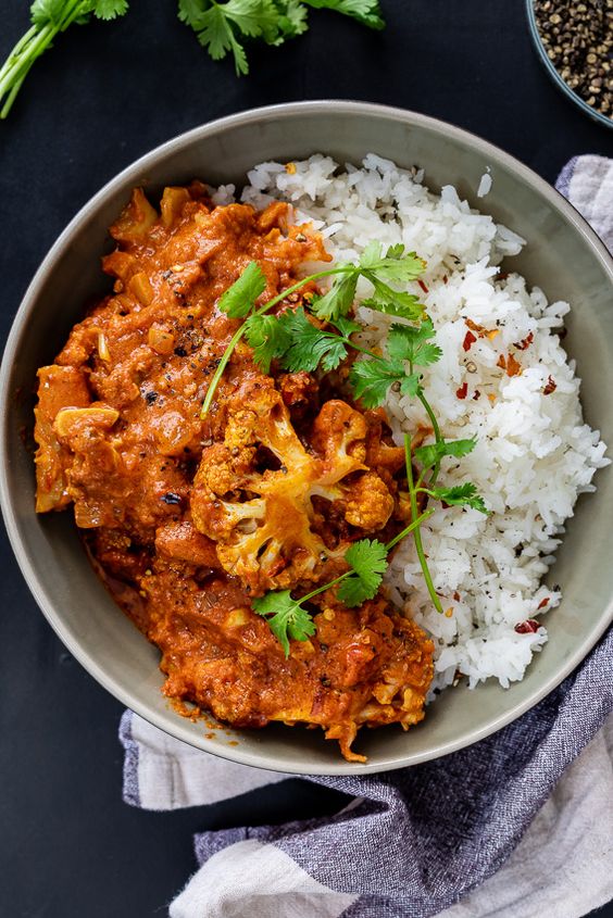 A bowl with cauliflower tiki masala on the left and rice on the right topped with cilantro.