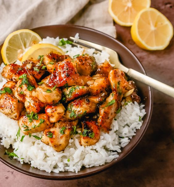 Hone chicken over rice in a bowl with a fork and lemons on the side.