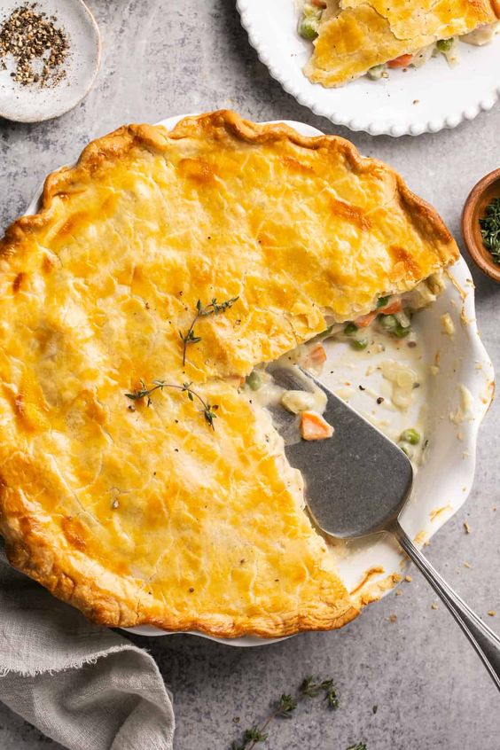 Chicken pot pie in a white pie dish with scolloped edges and a piece missing.