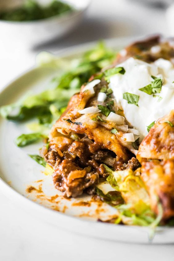 A white plate with two been enchiladas with sour cream.