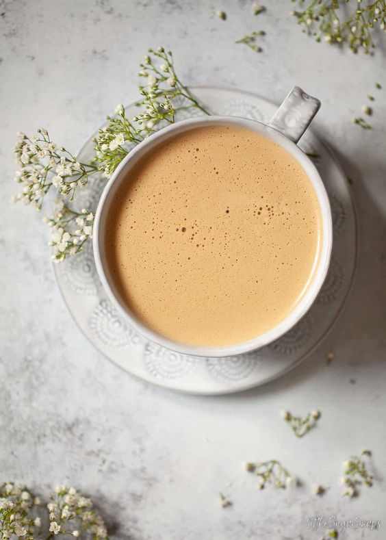 Honey Oat milk Latte in a cup with a spring of babies breath flower on the side of the cup.