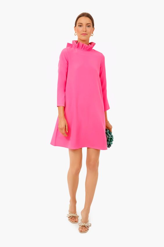 Woman wearing a pink dress with a ruffle at the neck. 