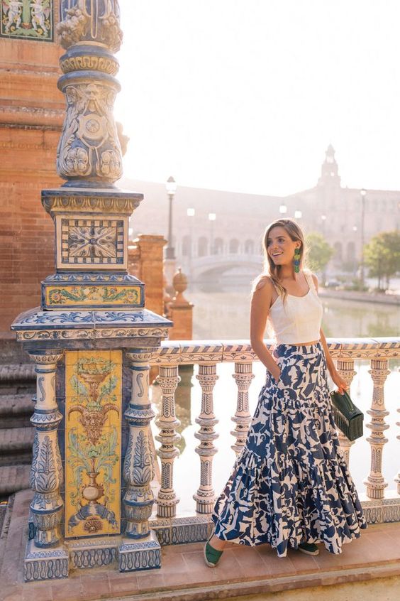 Woman in a white shirt and a blue and white skirt standing on a colorful tile bridge. 
