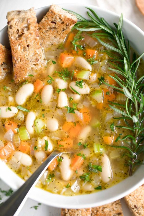 A bowl of ham, white bean and vegetable soup with 2 pieces of toast.