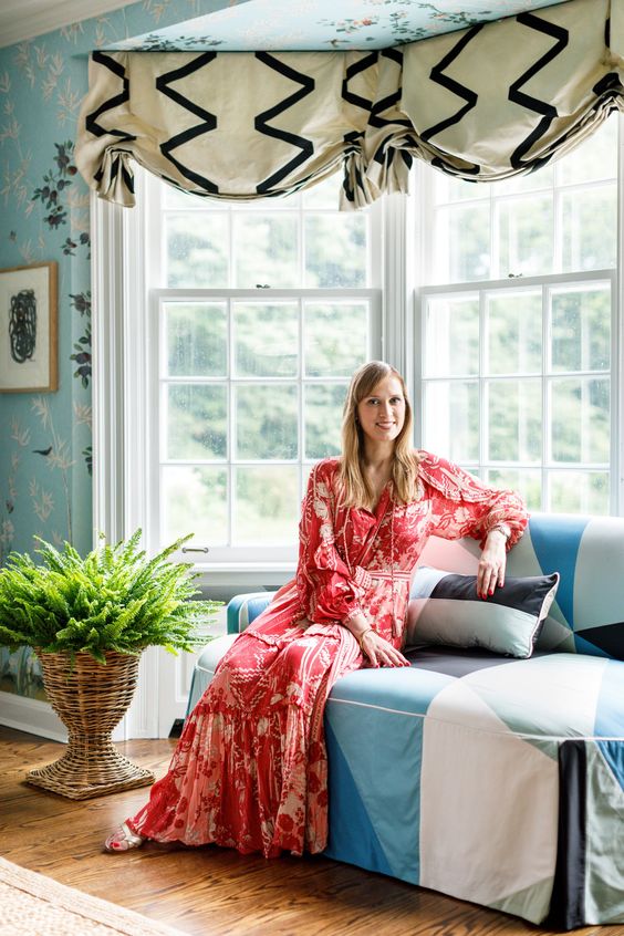 Woman sitting on a blue banquette wearing a red dress. 