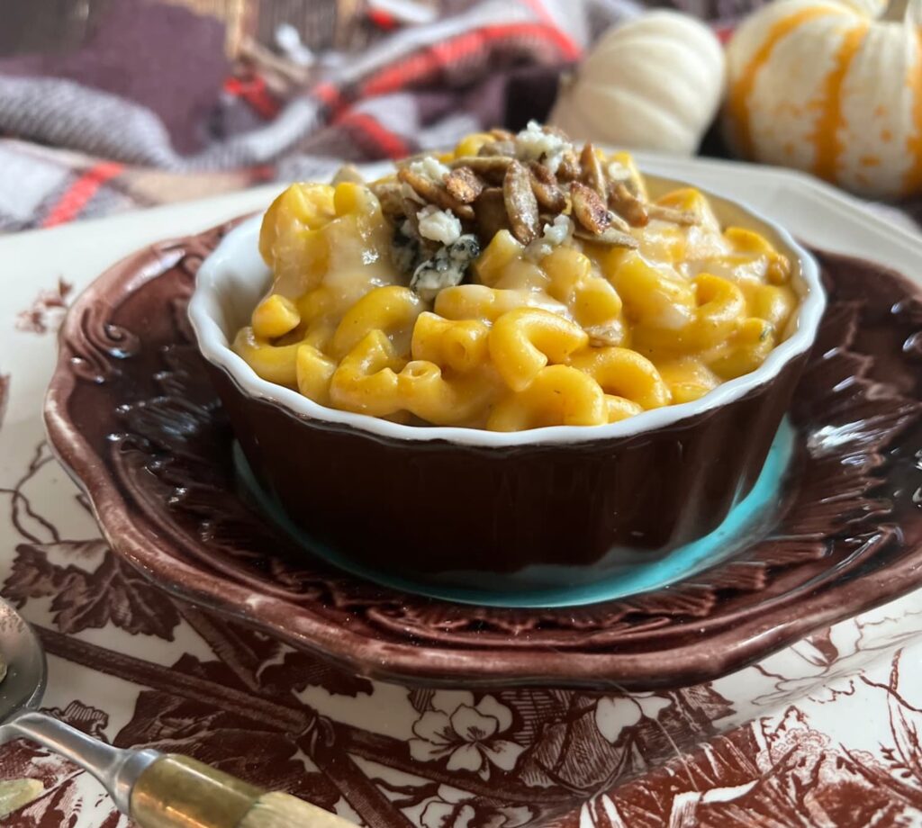 Pumpkin mac and cheese in a brown ramekin sitting on a transferware plate