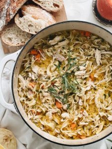 chicken noodle soup in a large pot with a few piece of bread on the side. 