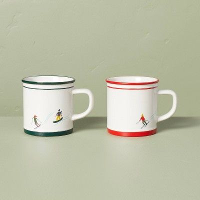 white mugs, one with red piping, one with green, both with little skiers.