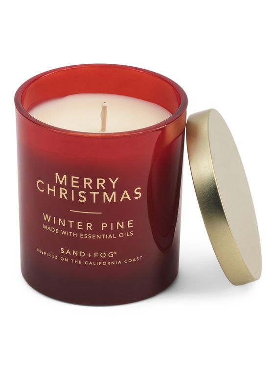 White candle in a red glass container with a gold lid leaning on the right side. 