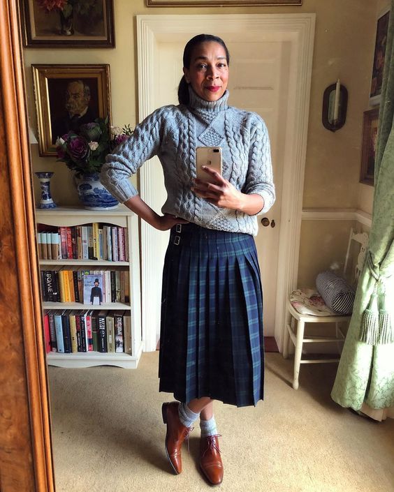 Paula Sutton wearing a gray sweater and a plaid skirt. 
