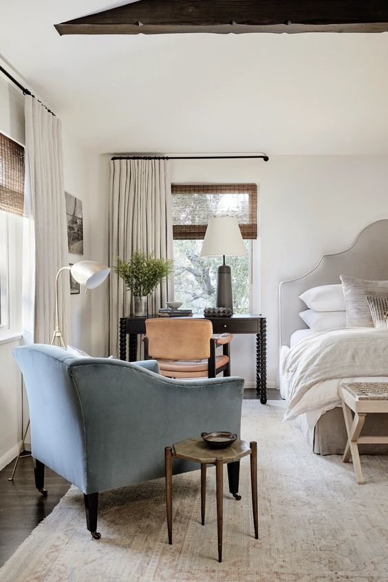 An airy white bedroom with a bed and a blue chair. 