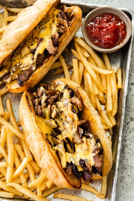 Philly Cheesesteak with French fries and ketchup on a sheet pan. 