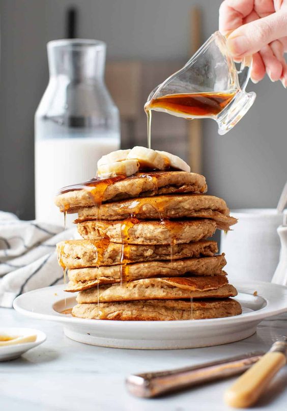 a stack of pancakes with syrup poured over the top and a glass bottle of milk