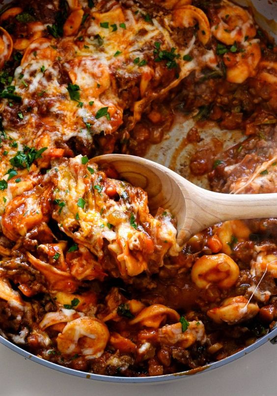 Baked Tortellini with Sausage in a pan scooped on a wooded spoon. 