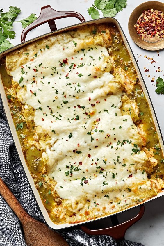 A white baking pan filled with green chicken enchiladas. 