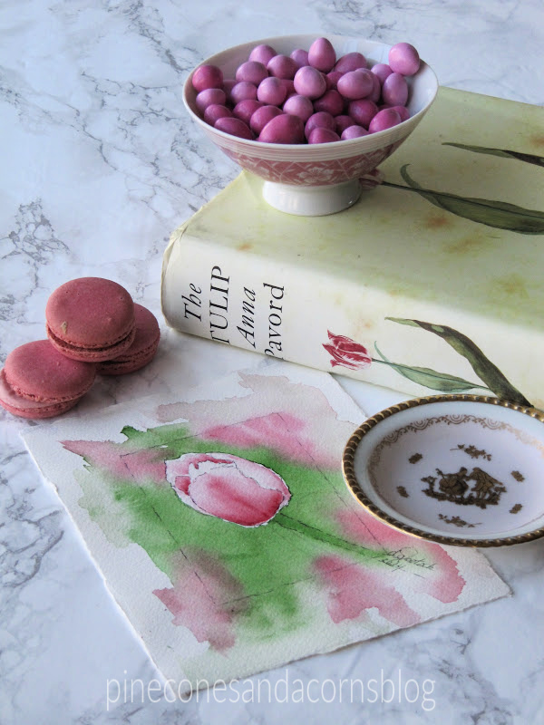 Spring tulip watercolor, pink macaroons, a tulip books and a bowl of pink candy.