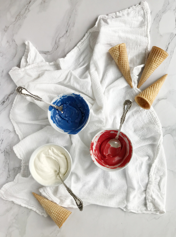 3 white bowls with red white and blue melted chocolate and 4 sugar cones laying on a white towel