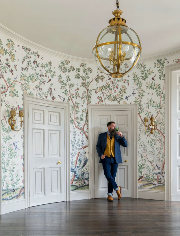 Gregg Penn Man with A Hammer, man standing with a glass of wine in a round foyer with chinoiserie wallpaper. 