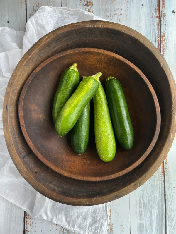 green zucchini piled into a stack of two antique dough bowls