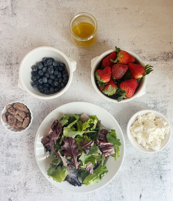 Ingredients for salad, spring greens, strawberries, blueberries, goat cheese and candied pecans.